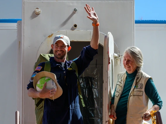 A person opens the door to a sealed habitat to as a second person exits waving and smiling.